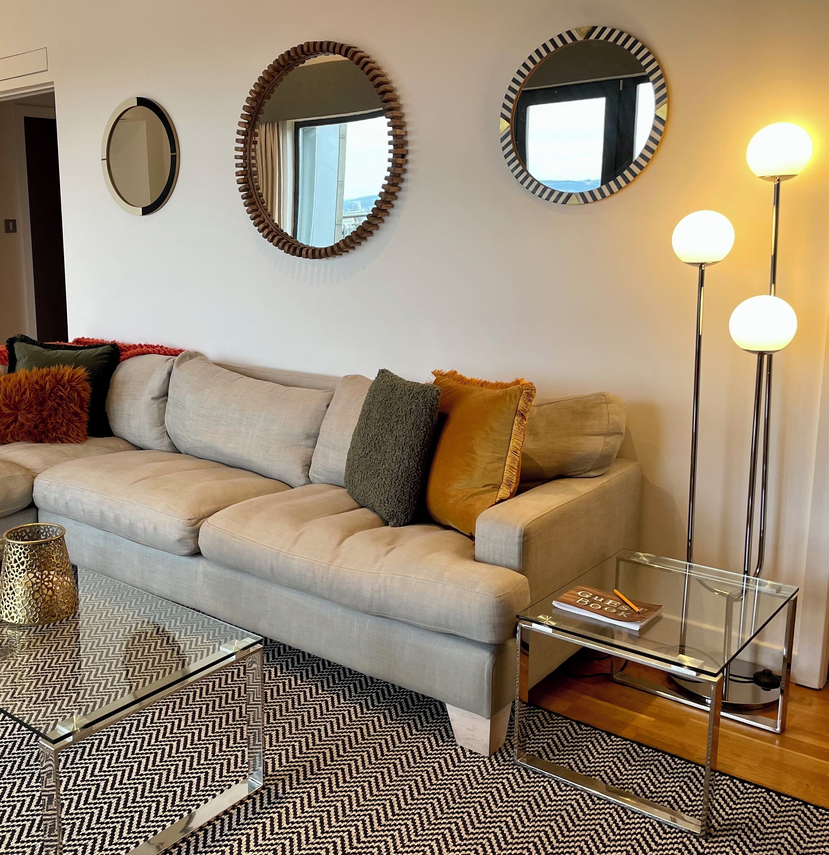 A living room with a sofa, two mirrors, a floor lamp, and a glass coffee table.