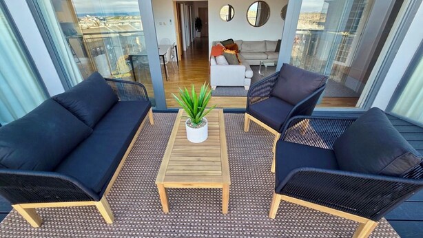 A balcony with two black sofas, a wooden table, and a potted plant.