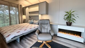 Ein modernes Schlafzimmer mit einem Bett, einem grauen Sessel, einem Kamin und einem Blumentopf.