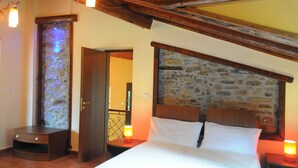 A bedroom with a stone headboard, a wooden nightstand with a lamp, and a small wooden bench.
