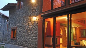 A stone building with a large glass door leading into a warmly lit interior.