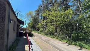 A paved path leading to a building with a brick facade, surrounded by trees and a clear sky. - Two Bedroom Cottage in Lumsden - Contractors (Huntly)