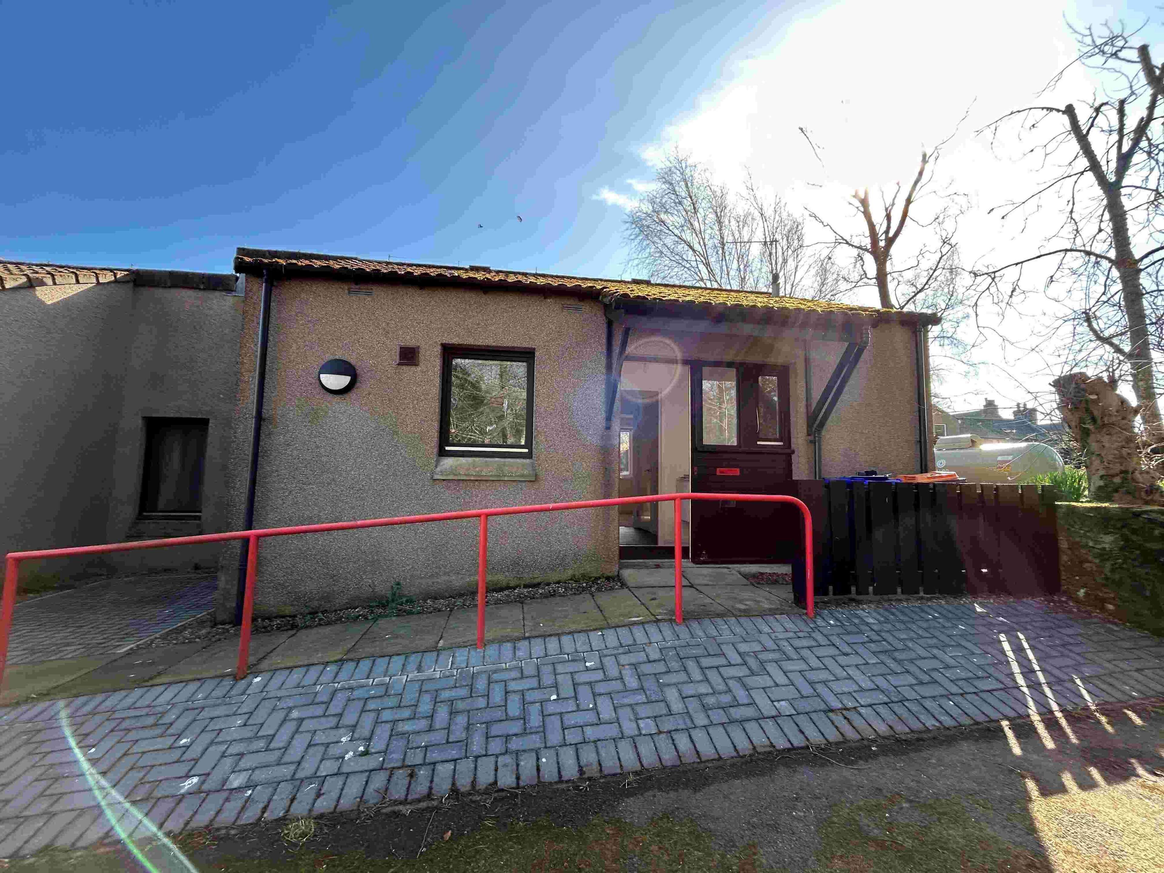 Un bâtiment avec une porte rouge, une petite fenêtre et une rambarde rouge à l’avant.