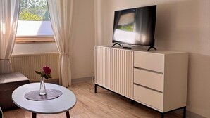 A room with a TV on a stand, a small table with a vase, and a window with curtains. - Cozy vacation apartment in a quiet location on the Prerower Strom (Prerow)