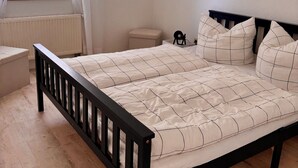 A bedroom with a bed, a nightstand, a window with curtains, and a radiator. - Cozy vacation apartment in a quiet location on the Prerower Strom (Prerow)