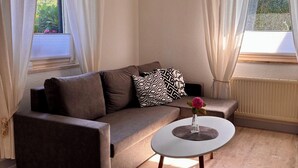 A modern living room with a brown sofa, a small round table with a vase, and a window with curtains. - Cozy vacation apartment in a quiet location on the Prerower Strom (Prerow)