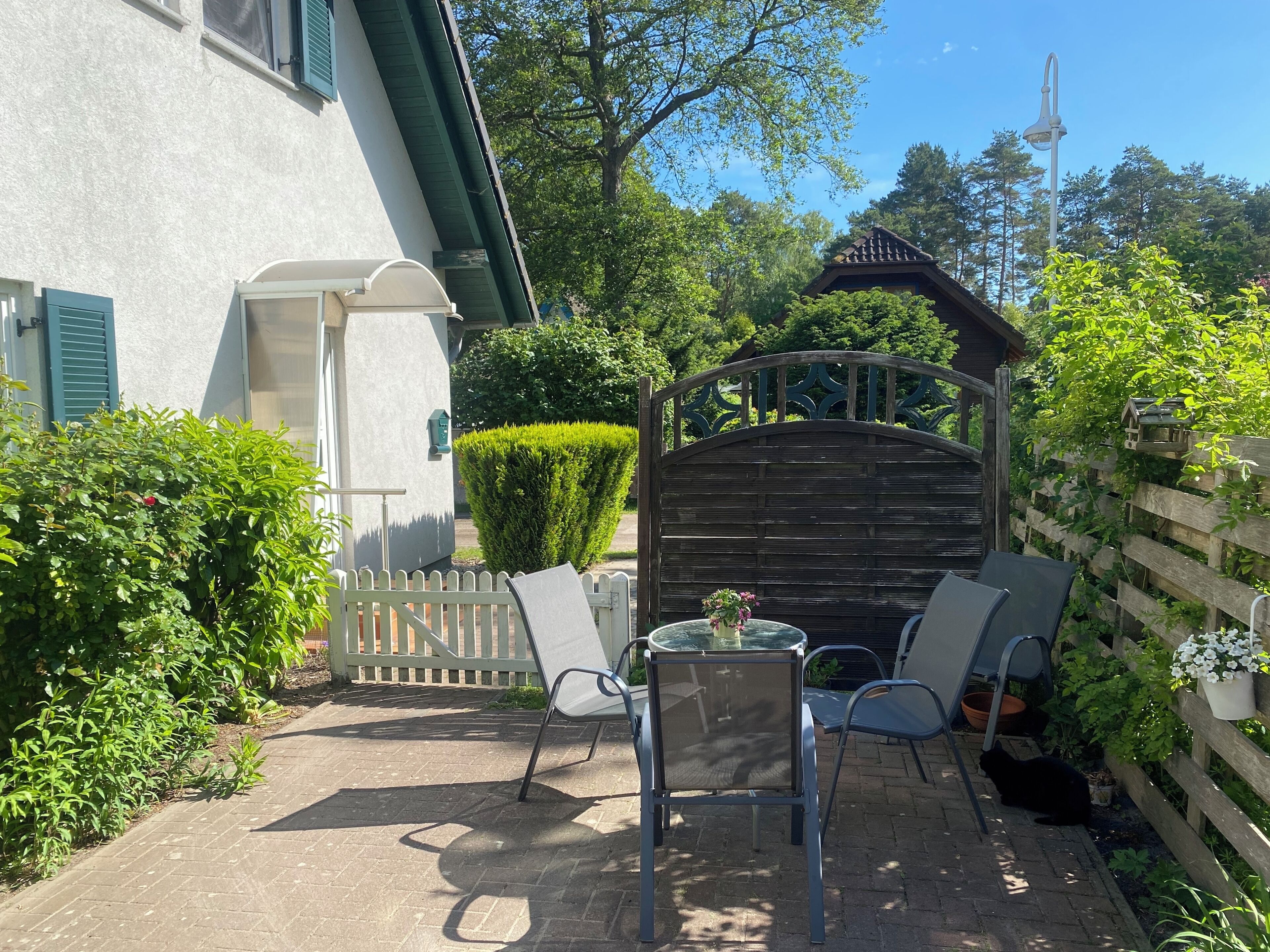 Une terrasse avec une table et des chaises, une porte en bois et une haie.