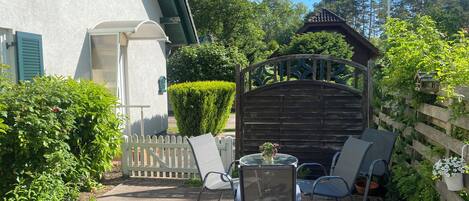 Une terrasse avec une table et des chaises, une porte en bois et une haie.