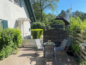 Un patio con una mesa, sillas, un portón de madera y un seto.