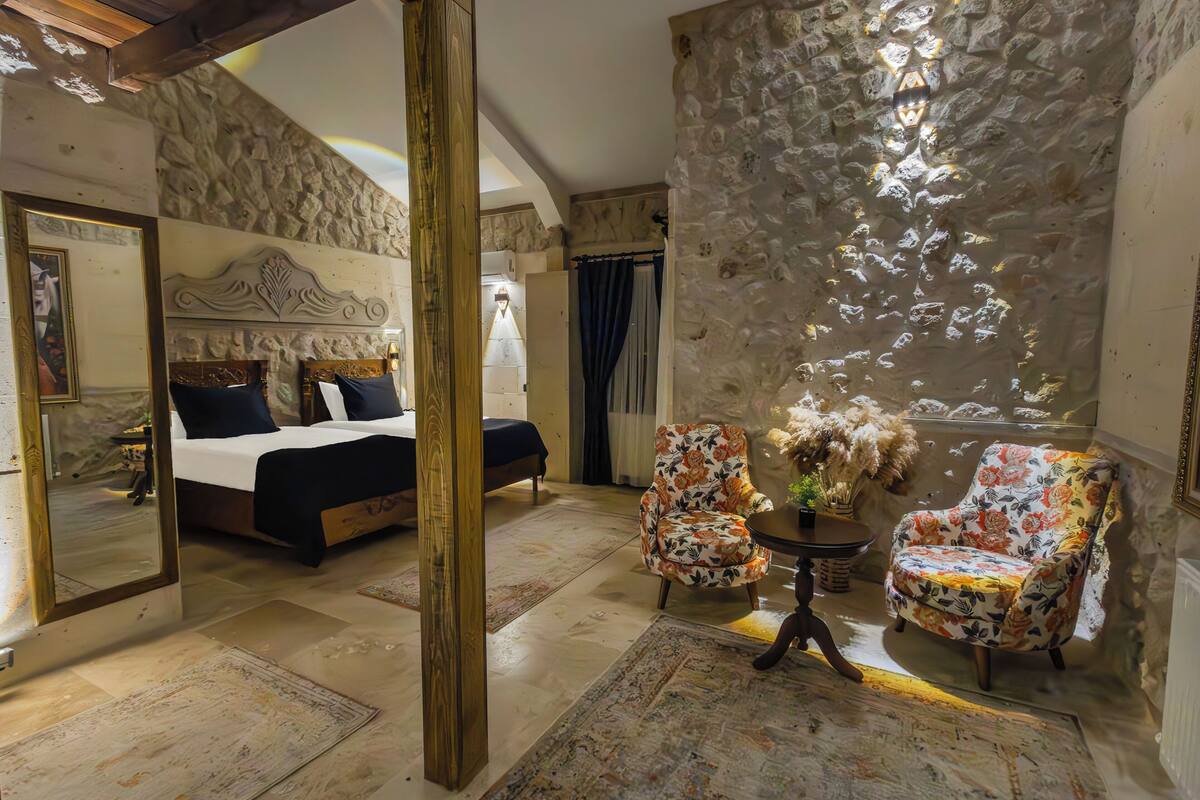 A bedroom with a large bed, a mirror, a floral armchair, and a small table with a vase.