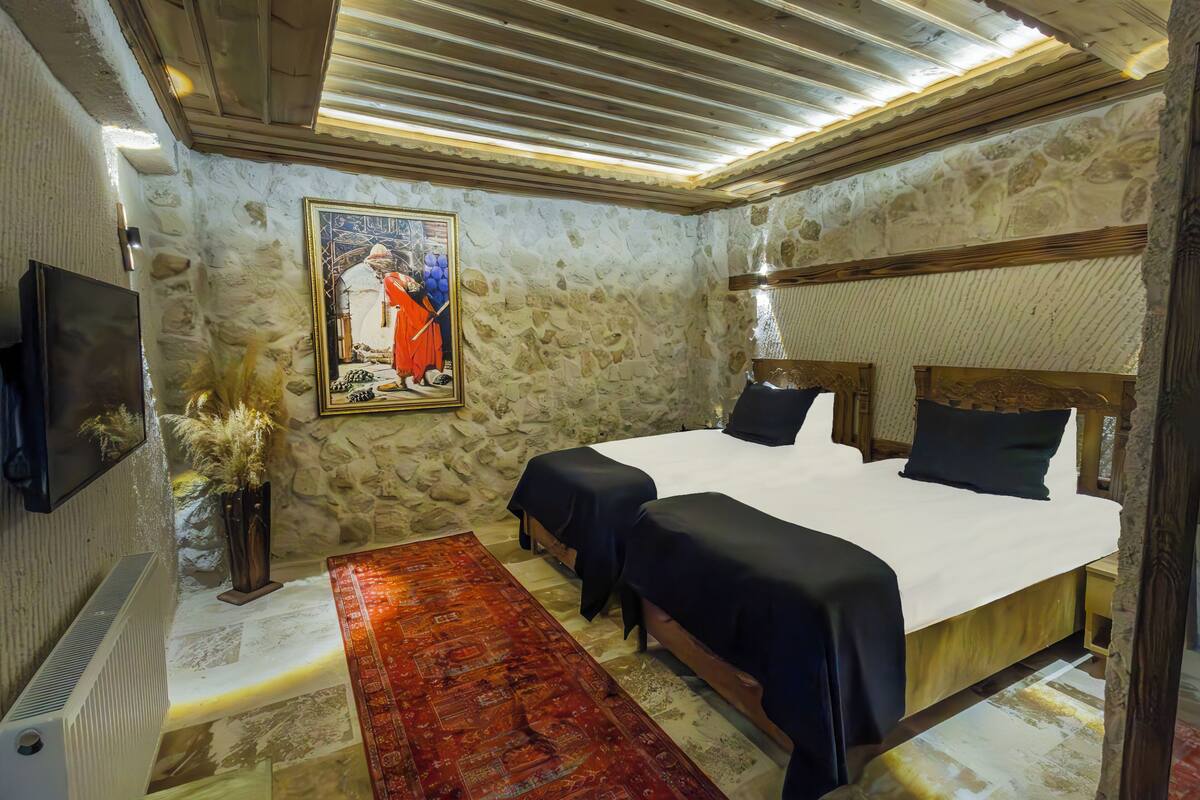 A room with a stone wall, a bed with black bedding, a red rug, and a framed picture on the wall.