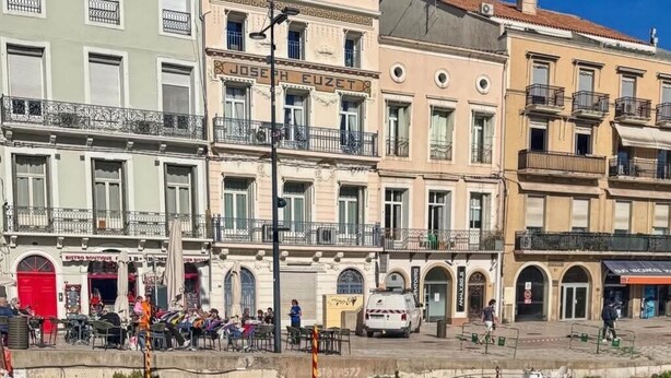 A waterfront with colorful boats docked, a café with outdoor seating, and a row of buildings with balconies. - Exceptional view of the sea from the popular Corniche district (Sète)