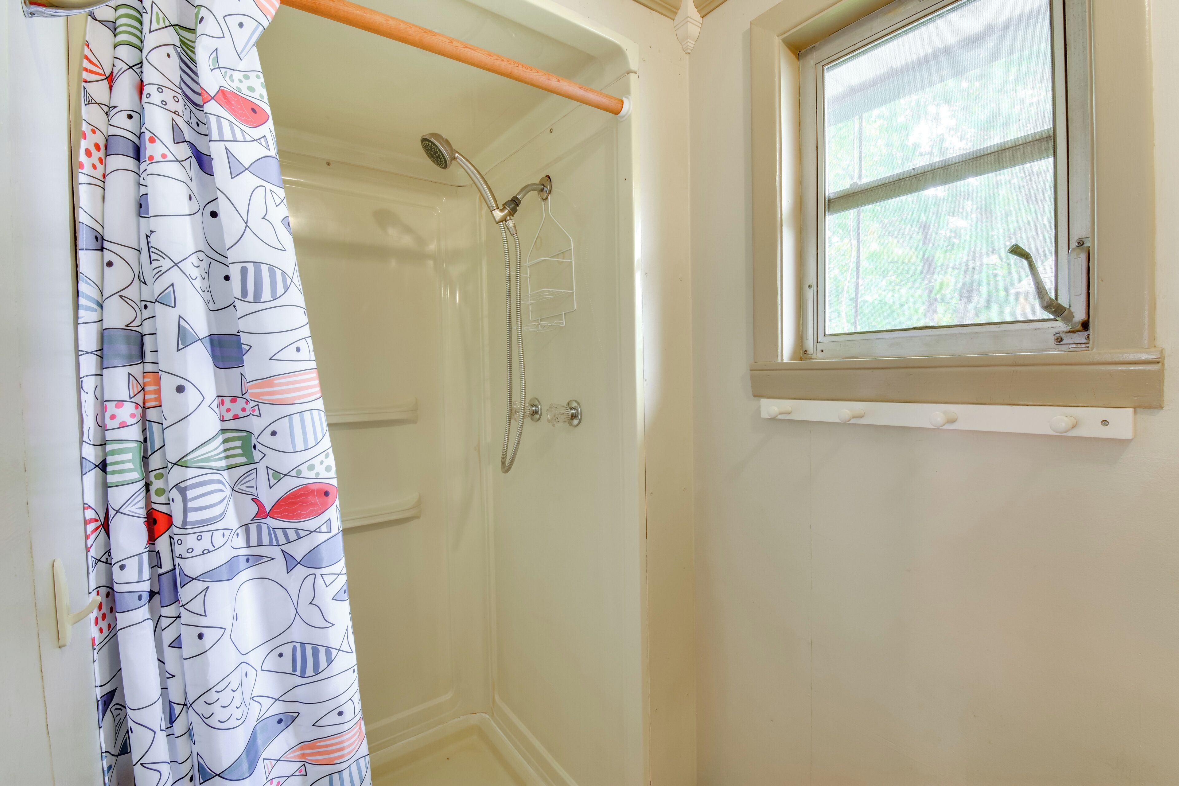 Une salle de bain avec une douche, une fenêtre et un rideau orné d’un motif de poissons.