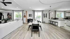 Una cocina moderna con armarios blancos, una isla central y una zona de comedor con una mesa grande y sillas.