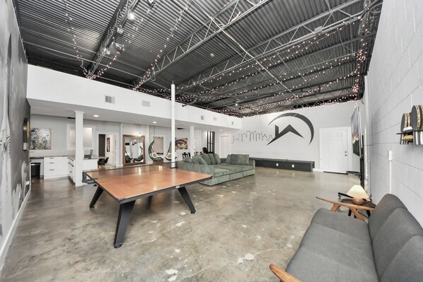 A spacious indoor area with a ping pong table, a gray sofa, and a large abstract wall art piece.