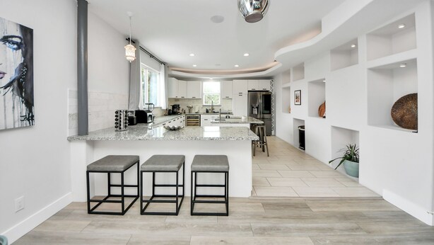 Una cocina moderna con una isla central, taburetes de bar y una lámpara colgante.