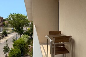 Ein Balkon mit Holztisch und Metallstuhl, der auf eine Straße mit Häusern und Grünflächen blickt.