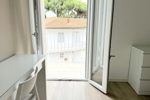Ein Zimmer mit einer Schiebetür zum Balkon, einem weißen Schreibtisch und einem weißen Schrank.