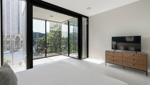 Een moderne slaapkamer met een groot schuifglasraam, een flatscreen televisie op een houten dressoir en een bed met een witte hoofdbord.