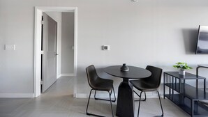Ein moderner Essbereich mit einem runden Tisch, zwei Stühlen, einem kleinen Topfpflanzen und einem an der Wand montierten Fernseher.