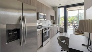 A modern kitchen with stainless steel appliances, a built-in oven, and a microwave. There is a dining area with a table and chairs, and a view of the outdoors through large windows. - Landing | Incredible 1BD in Fountain Heights (Birmingham)