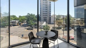 A room with a large window offering a view of a parking lot and buildings. There is a round table with two chairs and a vase on it. - Landing | Incredible 1BD in Fountain Heights (Birmingham)