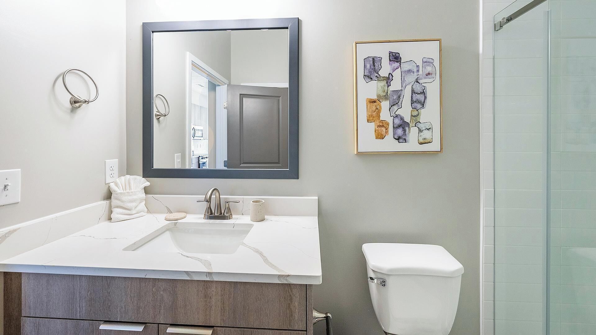 A bathroom with a white sink, a mirror, a toilet, and a framed artwork on the wall.