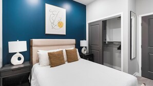 Una habitación de hotel con una cama, dos mesitas de noche con lámparas, una obra de arte en la pared y un armario.