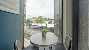A room with a round table and two chairs, a potted plant on the table, and a view of a parking lot and buildings outside.