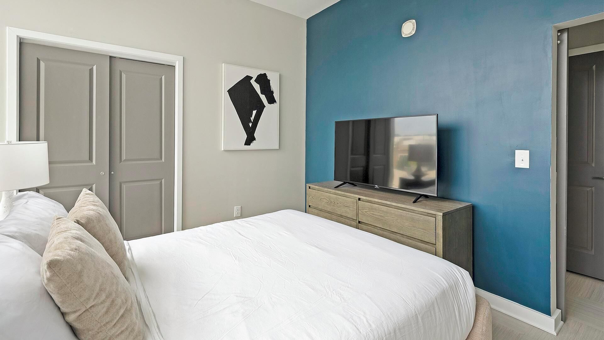 Un dormitorio con una cama, un televisor sobre un aparador de madera y una pared azul decorativa.