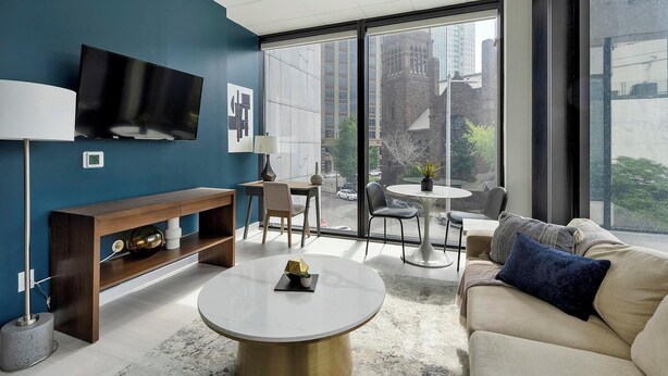 A modern living room with a sofa, coffee table, TV, and a balcony with a view of the city.