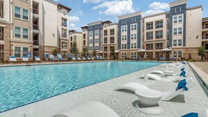 Une piscine avec des chaises longues et, en arrière-plan, un bâtiment à la façade en pierre.