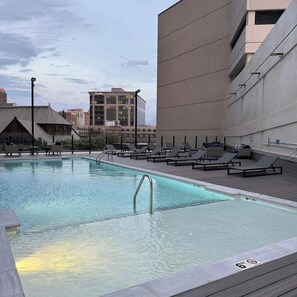 Una piscina en la azotea con sillones de descanso y vistas a la ciudad.