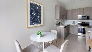 A modern kitchen with a dining area, featuring a white table, grey chairs, and a large abstract painting on the wall. - Landing | Modern 3BD in Fountain Heights (Birmingham)