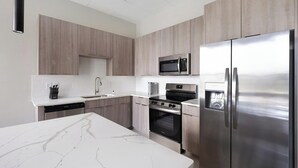 A modern kitchen with stainless steel appliances, a marble countertop, and wooden cabinetry. - Landing | Modern 3BD in Fountain Heights (Birmingham)