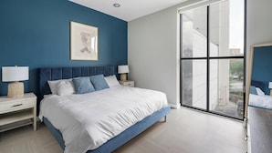 A modern bedroom with a large bed, two bedside tables, a framed artwork, and a large window offering a view of the outdoors. - Landing | Modern 3BD in Fountain Heights (Birmingham)