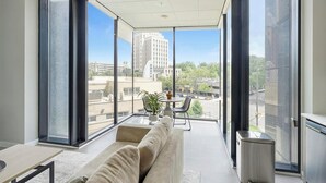 A modern living room with a large window, a sofa, a small table, and a potted plant. - Landing | Spectacular 1BD in Fountain Heights (Birmingham)