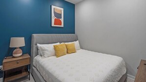 A bedroom with a bed, a nightstand, a lamp, and a painting on the wall. - Landing | Spectacular 1BD in Fountain Heights (Birmingham)