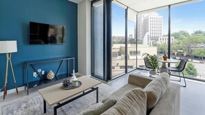A modern living room with a blue accent wall, a flat-screen TV, a sofa, a coffee table, and a large window offering a city view. - Landing | Spectacular 1BD in Fountain Heights (Birmingham)