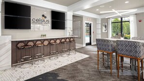 A modern bar area with a counter, bar stools, and a seating area with patterned chairs. - Landing | Stylish 2BD, Game Room, Gym (Charlotte)