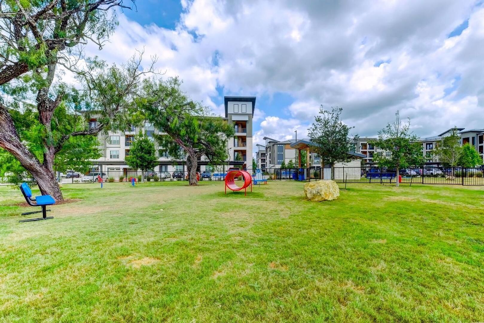 A grassy outdoor area with a playground, benches, and a large tree.
