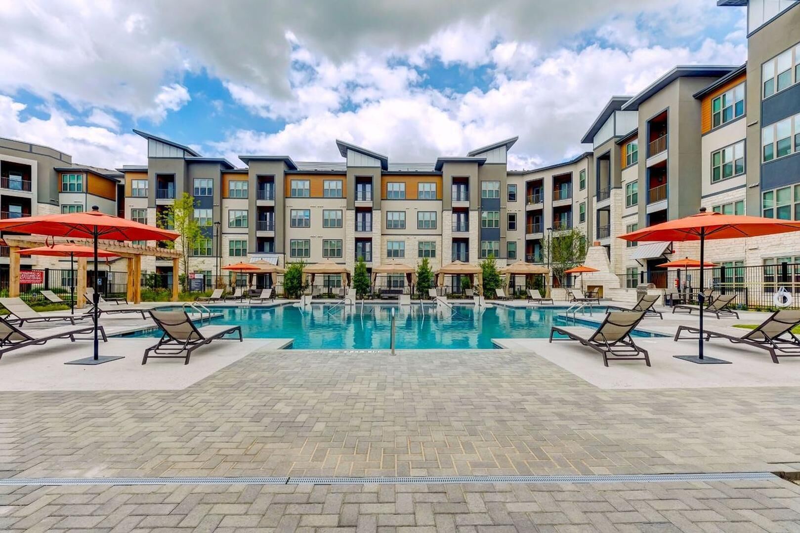 A modern hotel with a central swimming pool, lounge chairs, and umbrellas.