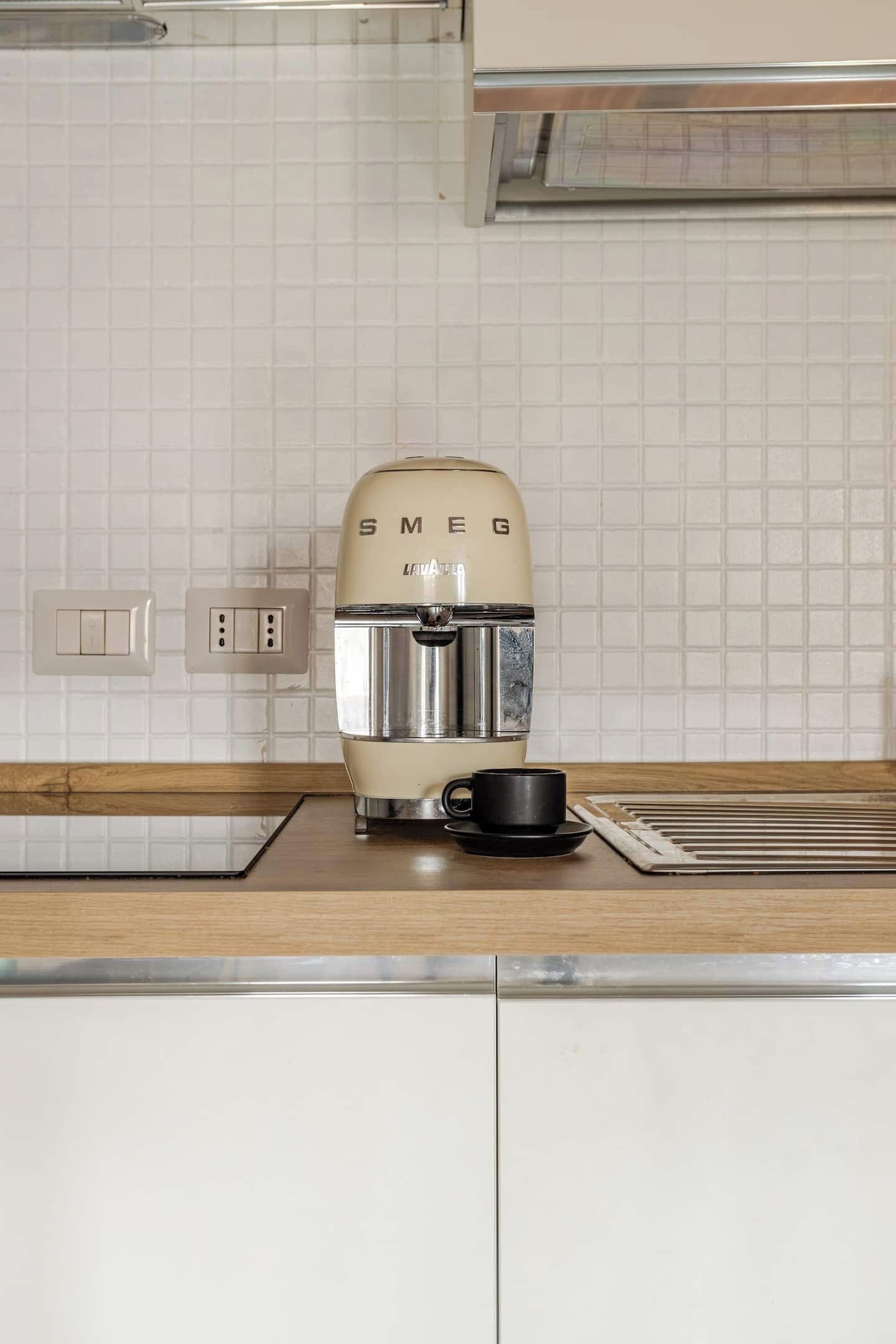 Et køkken med en vintage Smeg kaffemaskine, en sort kop og et flisebeklædt bagpanel.