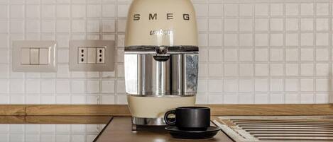 Een keuken met een vintage Smeg koffiezetapparaat, een zwarte mok en een betegelde achterwand.