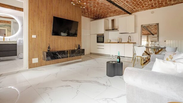 A modern living room with a TV, a fireplace, a dining area with a table set for two, and a kitchen in the background.