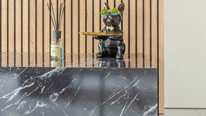 A reception desk with a black marble top, a wooden slatted wall behind, and a decorative dog figurine with sunglasses.
