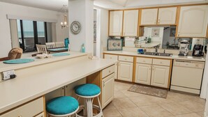 A kitchen with white cabinets, a sink, and a coffee maker. There are two stools with blue cushions. - Water's Edge Retreat-Direct Oceanfront @ Sandpoint, 2BR Oceanfront Pool (Daytona Beach)