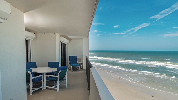 A balcony with a view of the beach, a table with chairs, and a door. - Water's Edge Retreat-Direct Oceanfront @ Sandpoint, 2BR Oceanfront Pool (Daytona Beach)