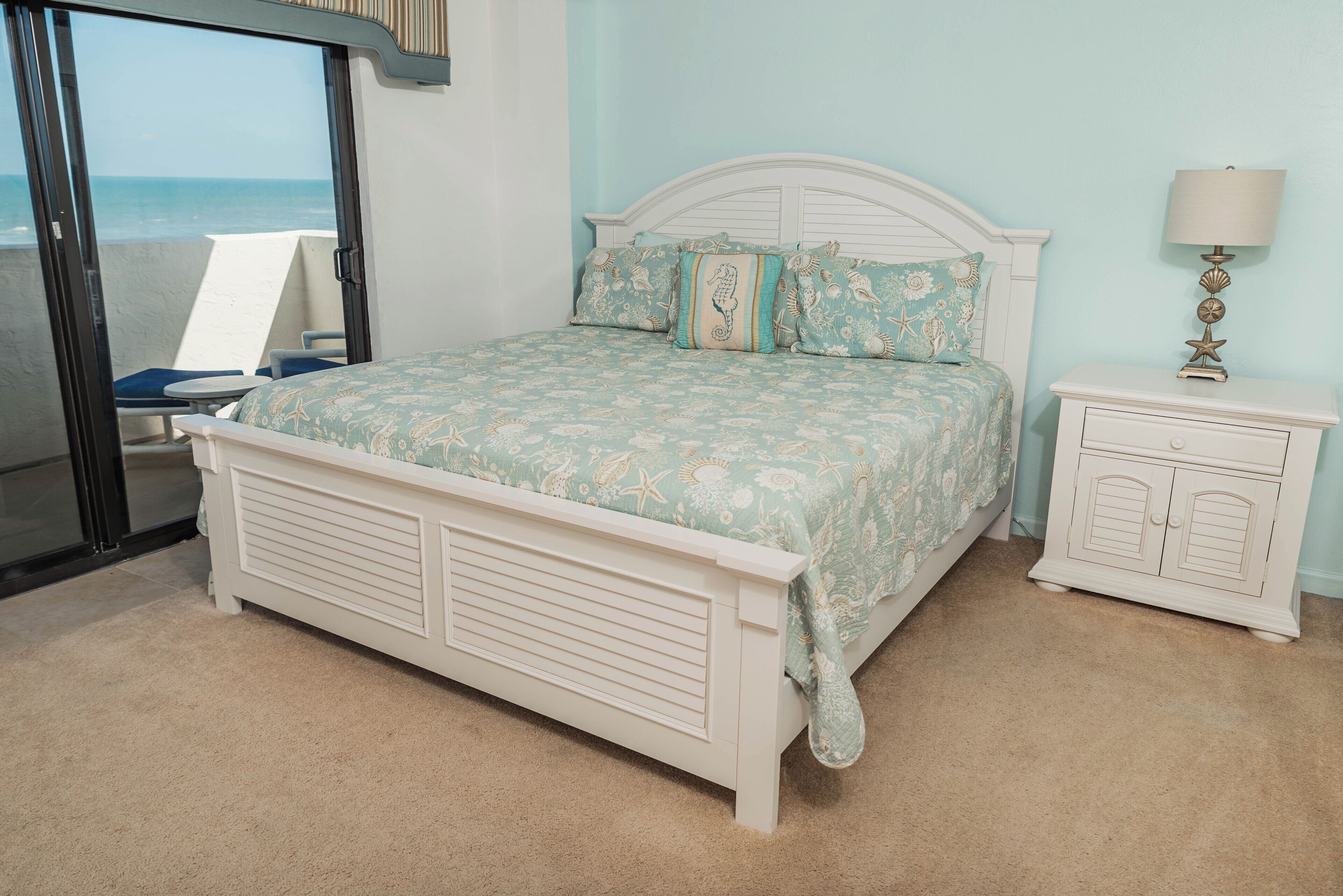 A bedroom with a bed, a nightstand, a chair, and a view of the ocean.