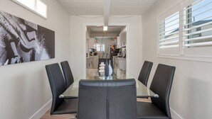 Un comedor moderno con una mesa de vidrio y sillas negras, que da acceso a una cocina con armarios blancos y vistas a un edificio.